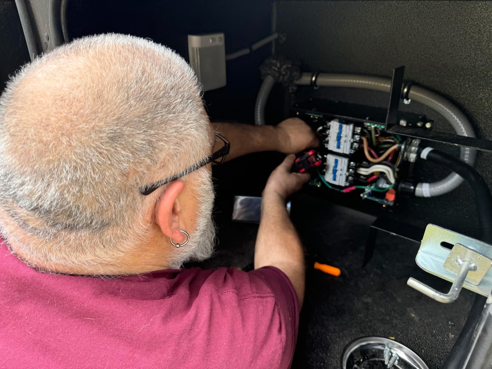 Oscar Alfonso working on electrical components inside an RV service compartment.